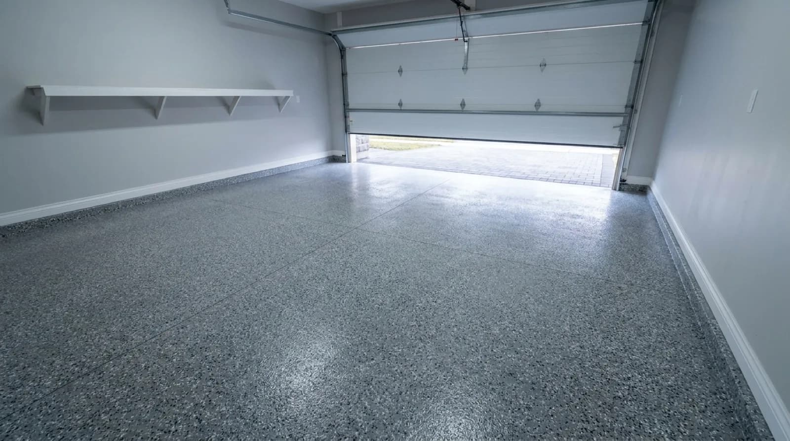 A double garage in a Toronto house with a finished speckled grey and charcoal flake floor catching light from an open garage door