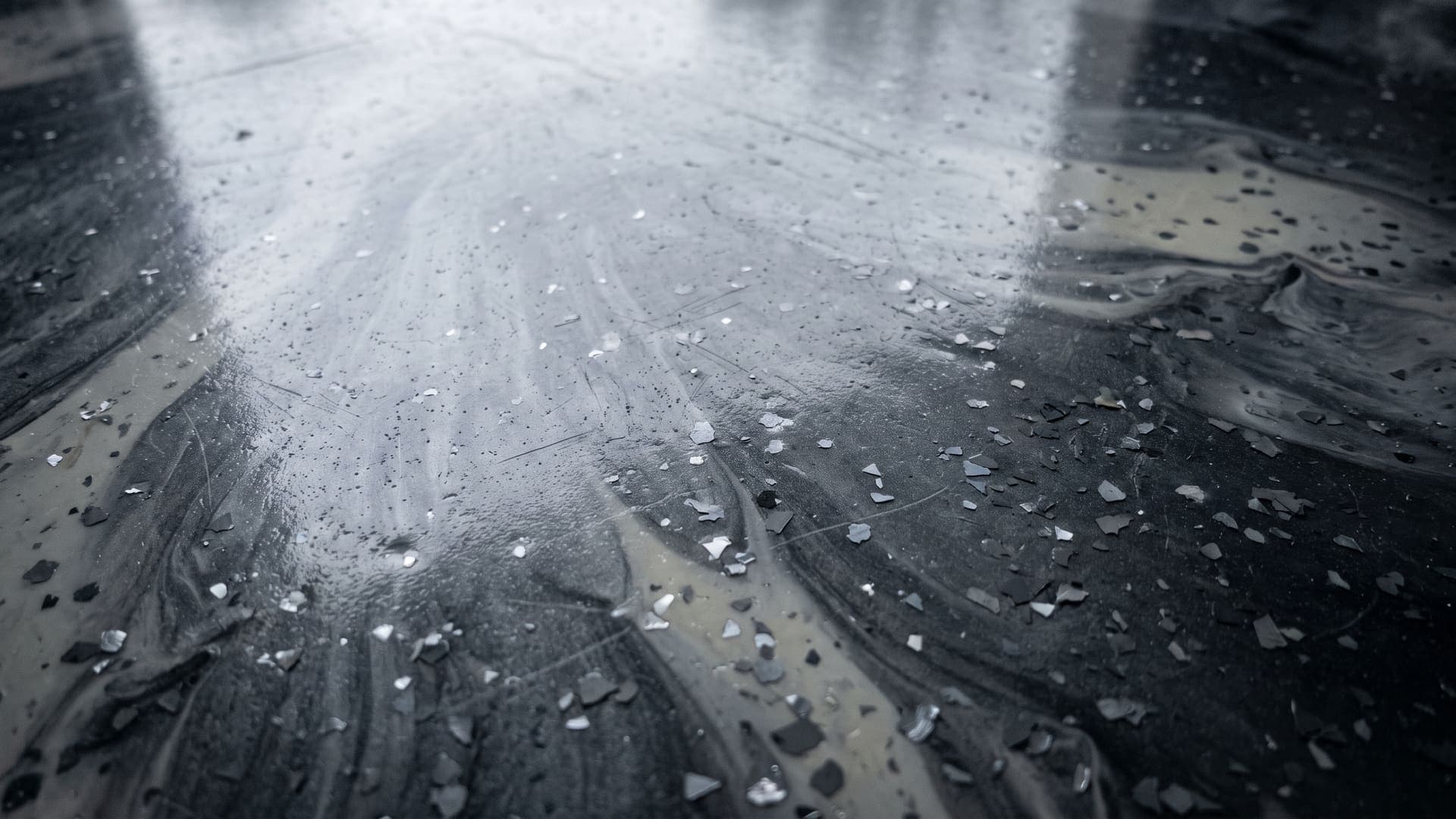 Close on a decorative metallic floor coating, graphite and pearl pigment marbled through the clear resin with vinyl flake chips caught in the pour, a broad soft light raking across the gloss